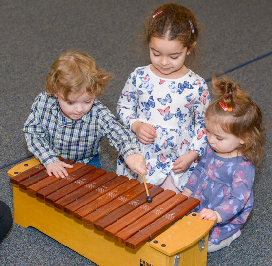 Three young toddlers, one boy and two girls, playing the xylophone.