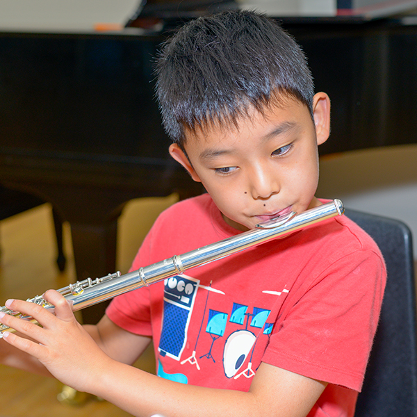 Young boy in red shirt playing the flute.